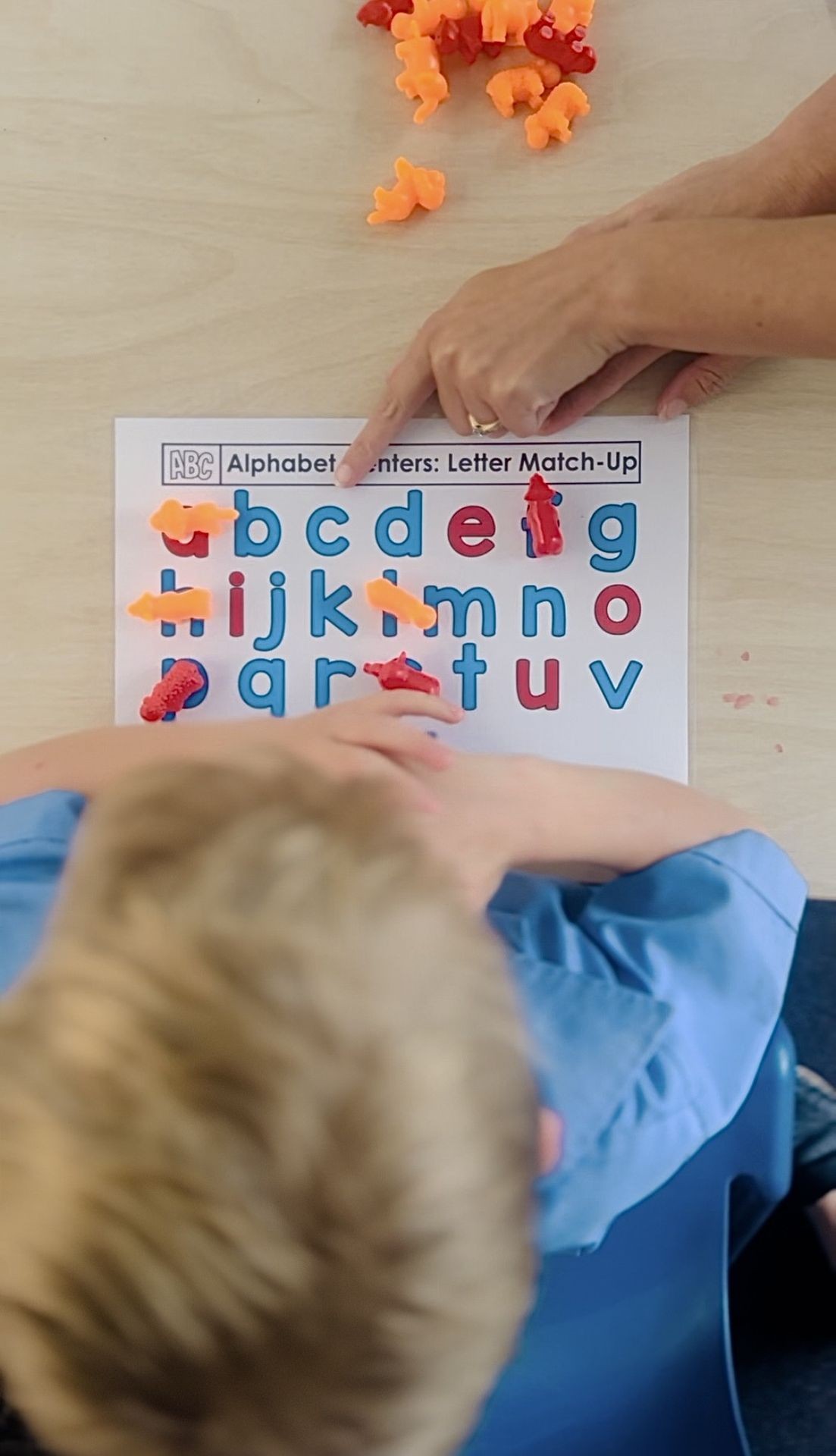 Child learning alphabet letters with colorful plastic pieces on a letter match-up worksheet.